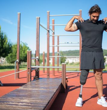 A man touching his shoulders while standing near the wooden platform